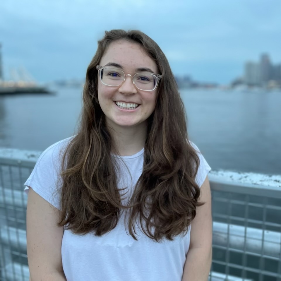 Photo of a white woman with brown hair standing in front of the Boston harbor